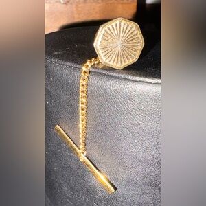 Gold-tone tie tack with sunburst engraved design and chain bar